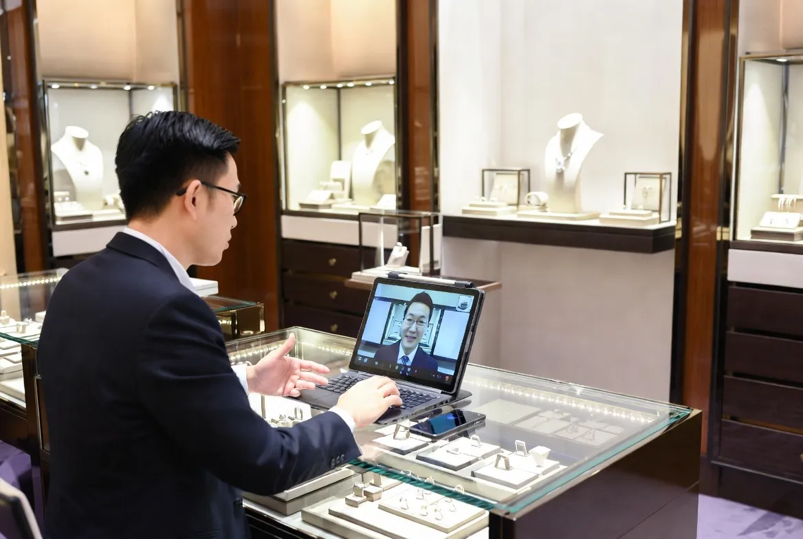 Luxury jewelry specialist conducting professional video consultation with customer on laptop in elegant boutique showroom with jewelry displays