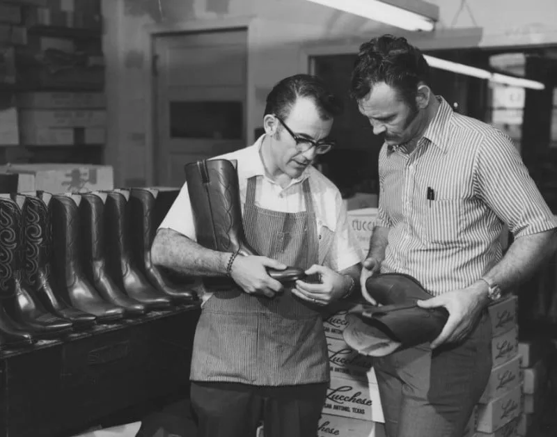 Two men examining a boot in a Lucchese stockroom, from the brand's archive.