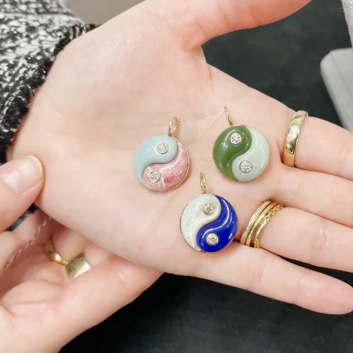 Three enamel yin-yang pendants held in an open hand at Ylang 23, over the dark velvet of the display table.